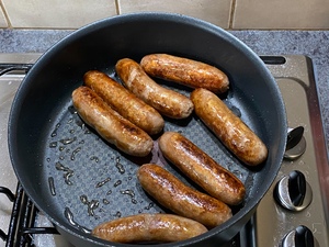 Beef sausages frying in casserole.
